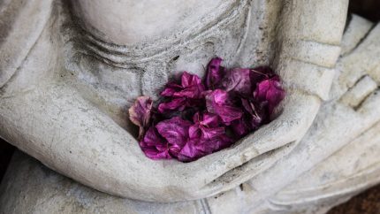 Concrete statue in meditation position holding purple flowers